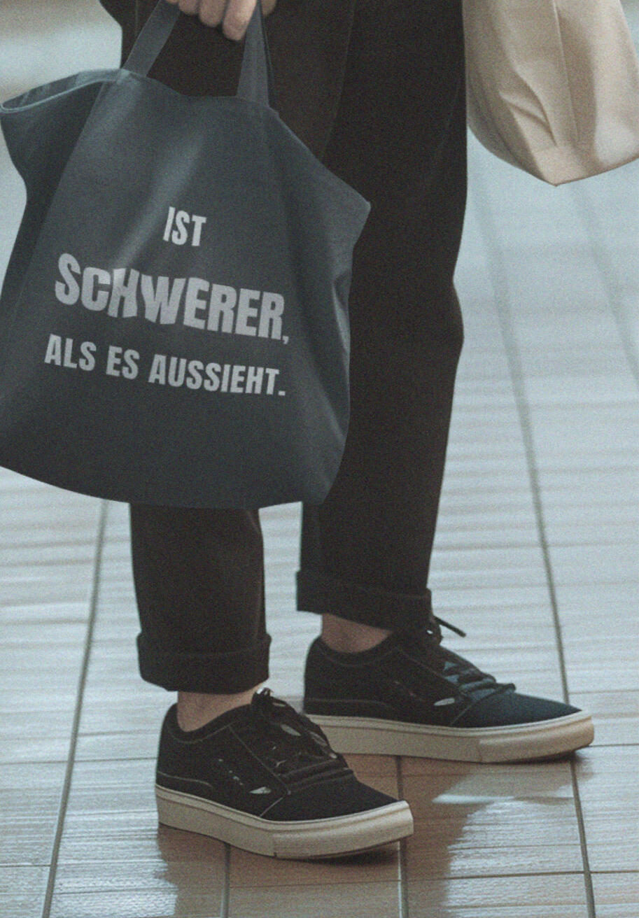 Person trägt schwarzen Stoffbeutel mit dem Satz „Ist schwerer als es aussieht“.